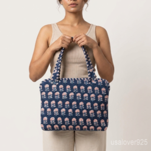 Close-up of the handcrafted blue floral block print detailing, dense quilted stitching texture lines, robust handle strap attachments, and clean zip track on an Indian cotton MacBook case.