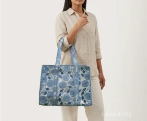 Close-up of the soothing blue floral prints, dense parallel line quilted stitching rows, and comfortable reinforced shoulder handles on an Indian cotton shopper bag.