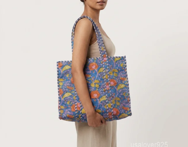 Close-up of the orange and yellow block print detailing, dense parallel line quilted stitching rows, supportive 5.5-inch gusset base, and handles on an Indian cotton tote bag.
