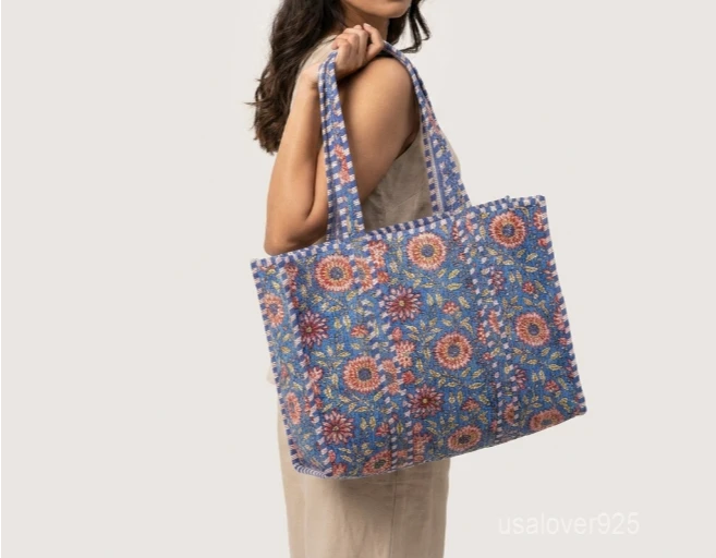 Close-up of the blue botanical floral print detailing, dense parallel line quilted stitching rows, interior valuables pocket, and comfortable 13-inch shoulder handles on an Indian cotton tote bag.
