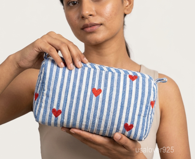 Close-up of the handcrafted blue striped print detailing, red heart motifs, dense quilted stitching texture lines, robust fabric edges, and clean zip track on an Indian cotton toiletry pouch.