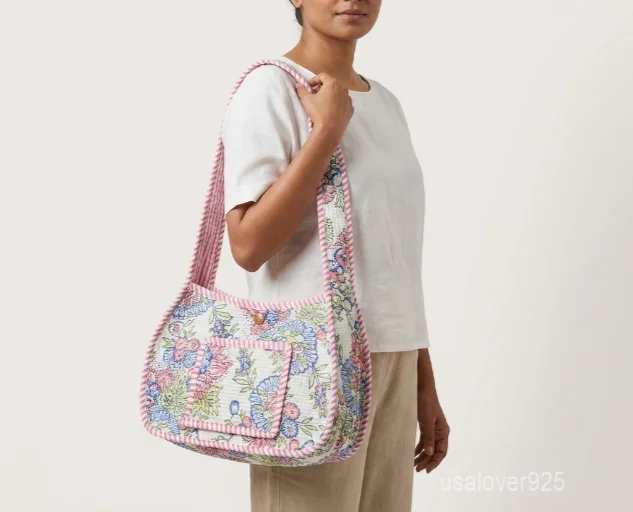Close-up of the pastel floral detailing, dense parallel line quilted stitching rows, front pocket with magnetic snap closure, and long shoulder strap on an Indian cotton purse.