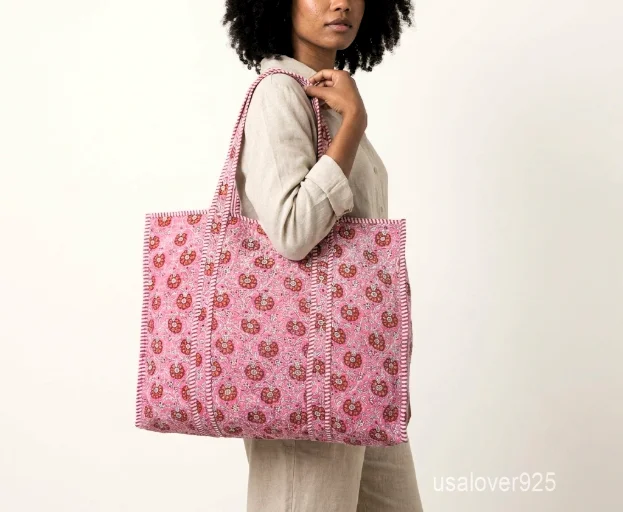 Close-up of the detailed embroidery accents, dense parallel line quilted stitching rows, contrast striped interior lining, inner slip pocket, and handles on an Indian cotton tote bag.