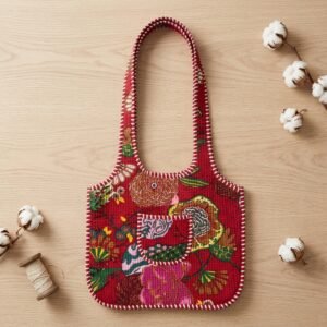 Close-up of the handcrafted vibrant red floral print detailing, traditional Kantha stitch running embroidery rows, dense quilted stitching texture lines, and robust handle strap attachments on an Indian cotton carryall tote.