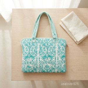 A creative professional carrying the Green Botanical Quilted Cotton Laptop Sleeve tote by the double handles, showcasing its slim profile and vibrant boho workspace style at a cafe.