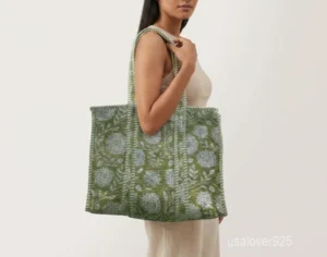 Close-up of the fresh green leaf prints, dense parallel line quilted stitching rows, and comfortable reinforced striped handles on an Indian cotton shopper bag.