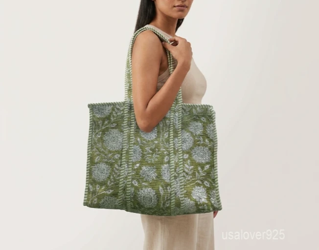 Close-up of the fresh green leaf prints, dense parallel line quilted stitching rows, and comfortable reinforced striped handles on an Indian cotton shopper bag.