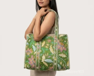 Close-up of the fresh green leaf prints, dense parallel line quilted stitching rows, and comfortable reinforced shoulder handles on an Indian cotton shopper bag.