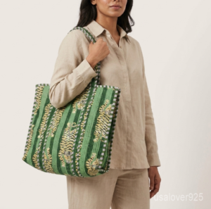 A shopper carrying the Green Tiger Quilted Tote Bag by the wide straps, showcasing its generous packing capacity and vibrant bohemian accessory style at a farmers market.