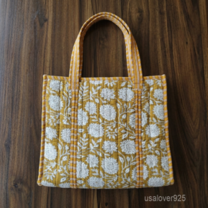 Close-up of the handcrafted mustard yellow floral block print detailing, dense quilted stitching texture lines, robust handle strap attachments, and neatly tailored soft fabric edges on an Indian cotton carryall caddy.