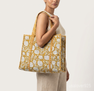 Close-up of the handcrafted mustard yellow floral block print detailing, dense quilted stitching texture lines, robust handle strap attachments, and neatly tailored soft fabric edges on an Indian cotton carryall caddy.