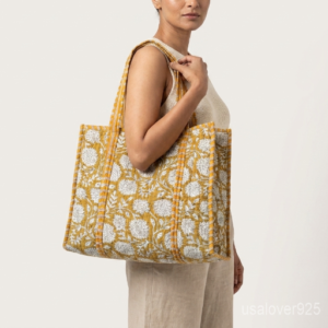 Close-up of the handcrafted mustard yellow floral block print detailing, dense quilted stitching texture lines, robust handle strap attachments, and neatly tailored soft fabric edges on an Indian cotton carryall caddy.