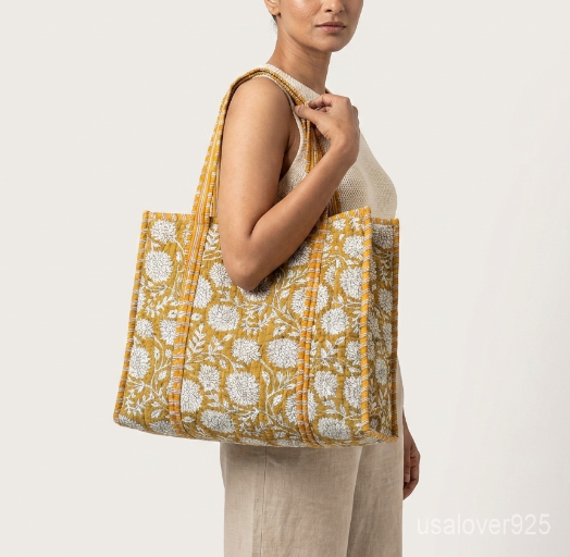 Close-up of the handcrafted mustard yellow floral block print detailing, dense quilted stitching texture lines, robust handle strap attachments, and neatly tailored soft fabric edges on an Indian cotton carryall caddy.