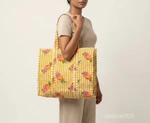 Close-up of the orange botanical floral print, dense parallel line quilted stitching, and comfortable 13-inch handle drop straps on an Indian cotton shopper bag.