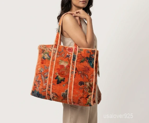 Close-up of the orange botanical print, dense parallel line quilted stitching rows, funky striped lining with an inner pocket, and comfortable shoulder handles on an Indian cotton tote bag.