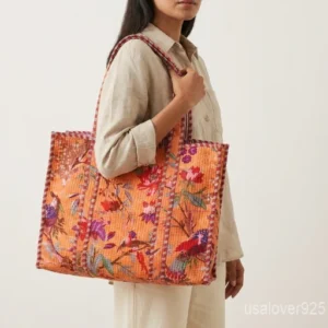 Close-up of the orange block print detailing, dense parallel line quilted stitching rows, and comfortable 13-inch shoulder handles on an Indian cotton tote bag.