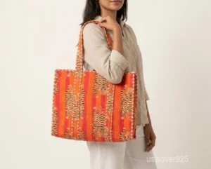 Close-up of the orange block print detailing, dense parallel line quilted stitching rows, and comfortable 13-inch shoulder handles on an Indian cotton tote bag.