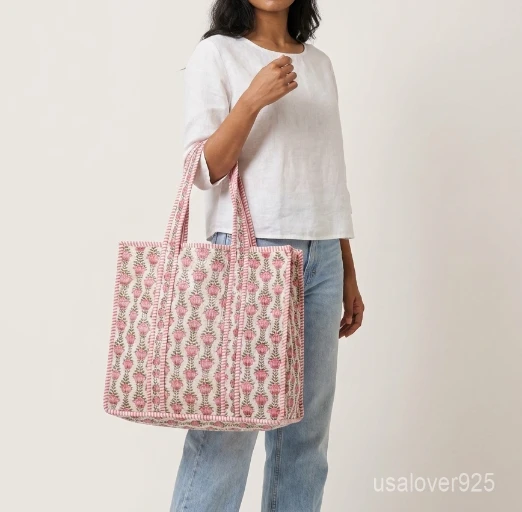 Close-up of the handcrafted pink floral block print detailing, contrasting striped handles pattern, dense Kantha-style quilted stitching lines, and neatly tailored edges on an Indian cotton carryall tote.