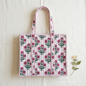 A woman carrying the Pink Floral Quilted Tote Bag by the wide straps, showcasing its light padded structure and vibrant boho accessory style at an outdoor market.