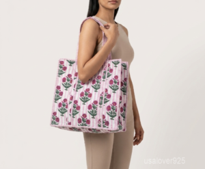 Close-up of the handcrafted pink floral block print detailing, soft striped background pattern, dense quilted stitching texture lines, robust handle attachments, and neatly tailored edges on an Indian cotton carryall tote.