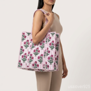 Close-up of the handcrafted pink floral block print detailing, soft striped background pattern, dense quilted stitching texture lines, robust handle attachments, and neatly tailored edges on an Indian cotton carryall tote.