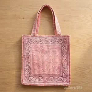 A person holding a square Pink Paisley Kantha Quilted Cotton Tote Bag by its double handles during a casual weekend outing.