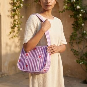 Close-up of the handcrafted red heart and purple stripe layout, dense quilted stitching lines, robust strap attachments, and zip slider on an Indian cotton carryall makeup tote.