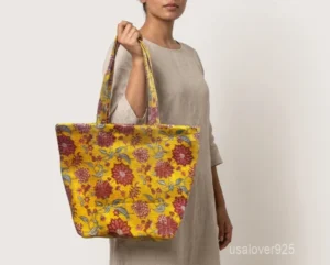 Close-up of the yellow floral block print detailing, dense parallel line quilted stitching rows, built-in magnetic snap lock, and reinforced handles on an Indian cotton tote bag.