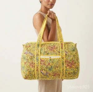 Close-up of the handcrafted yellow floral block print detailing, dense quilted stitching texture lines, robust handle attachments, external front zip slot, and adjustable strap strap hook on an Indian cotton weekender tote.