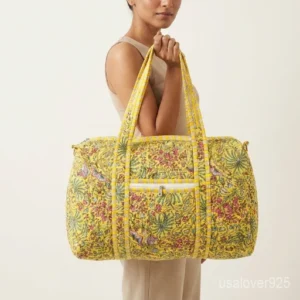 Close-up of the handcrafted yellow floral block print detailing, dense quilted stitching texture lines, robust handle attachments, external front zip slot, and adjustable strap strap hook on an Indian cotton weekender tote.