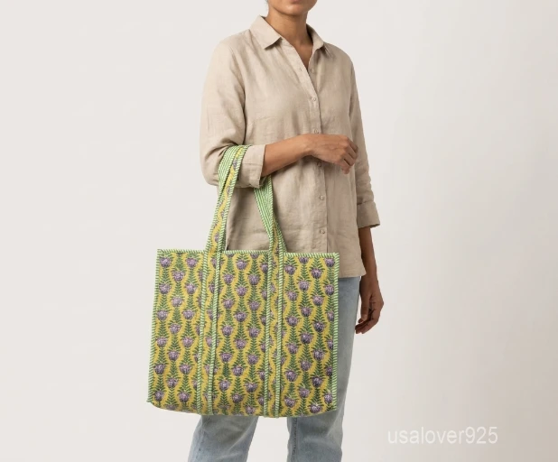 Close-up of the fresh green leaf prints, dense parallel line quilted stitching rows, and comfortable reinforced shoulder handles on an Indian cotton shopper bag.