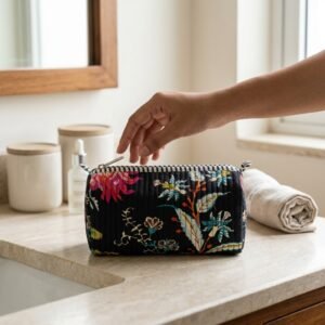A traveler arranging the three pieces of the Black Chintz Quilted Toiletry Bag Set on a modern bathroom vanity counter, displaying the large, medium, and small sizes filled with cosmetic brushes and skincare bottles.