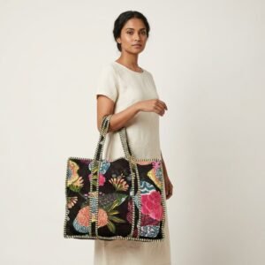 A shopper carrying the Black Floral Quilted Shoulder Tote Bag by the wide straps under the arm, showcasing its generous packing capacity and elegant bohemian accessory style at an outdoor market.