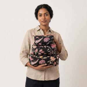 A traveler arranging the three pieces of the Black Floral Quilted Toiletry Bag Set on a modern bathroom vanity counter, displaying the large, medium, and small sizes filled with cosmetic brushes and skincare bottles.