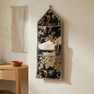 An interior room setup showing the Black Floral Quilted Wall Hanging Organizer near a wooden desk, showcasing its space-saving capacity and elegant vintage room holder style.