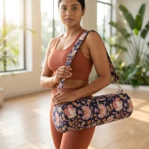 a woman in an indoor fitness studio holds the Blue Kalamkari Quilted Cotton Yoga Mat Bag over her shoulder using the matching adjustable strap, showcasing its practical utility and elegant bohemian style.