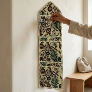 An interior room setup showing the Kalamkari Fabric Wall Hanging Organizer near a wooden desk, showcasing its space-saving capacity and elegant beige bird decor holder style.
