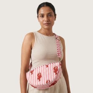 A traveler wearing the Lobster Print Quilted Crossbody Bag across the chest as a sling, showcasing its compact packing capacity and playful bohemian accessory style during an outdoor music festival.