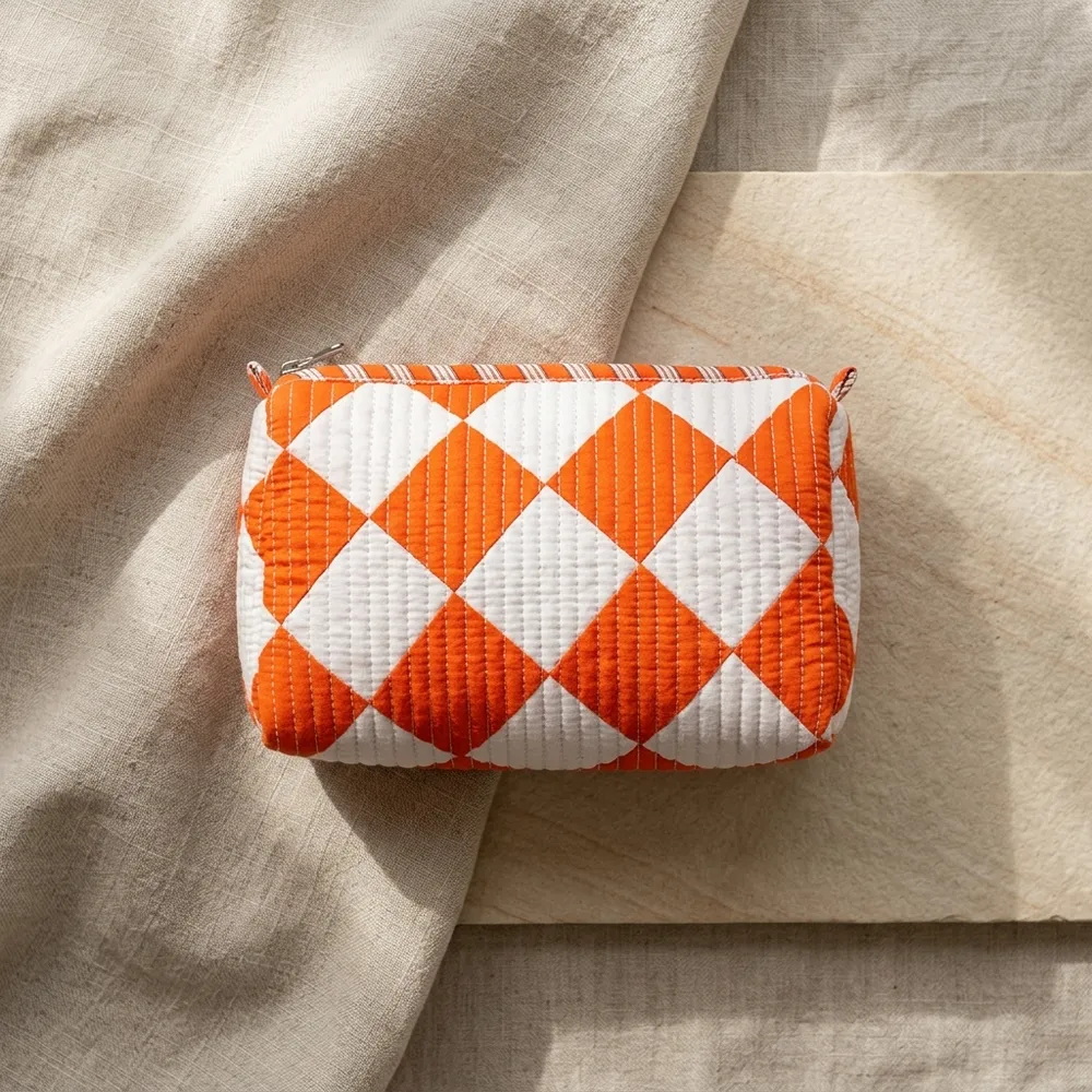 Close-up of the handcrafted orange diamond geometric print detailing, dense quilted stitching texture lines, robust zipper attachment, and clean water-resistant lining on the cotton cosmetic pouch.