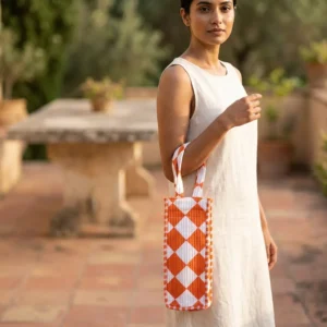 A scenic picnic setup featuring the Orange Diamond Quilted Water Bottle Bag holding a glass bottle on a blanket, showing its use as a premium travel drink carrier.