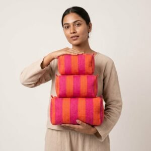 A traveler arranging the three pieces of the Orange Pink Striped Quilted Toiletry Bag Set on a modern bathroom vanity counter, displaying the large, medium, and small sizes filled with cosmetic brushes and skincare bottles.