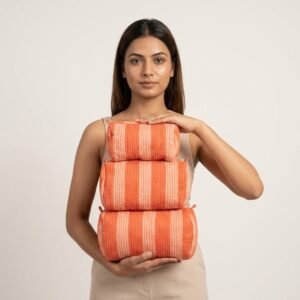 A traveler arranging the three pieces of the Orange Striped Quilted Toiletry Bag Set on a modern bathroom vanity counter, displaying the large, medium, and small sizes filled with cosmetic brushes and skincare bottles.