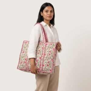 A shopper carrying the Pink Floral Quilted Tote Bag by the wide straps, showcasing its generous packing capacity and elegant large shoulder handbag style at an outdoor farmers market.