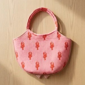 Close-up of the handcrafted pink coastal lobster print detailing, dense quilted tracking lines, clean magnetic snap button, and interior slip pocket on the cotton handbag.