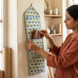 A home office wall showcasing the Quilted Yellow Floral Cotton Hanging Wall Organizer mounted beside a desk, displaying the 3 storage pockets filled with writing notebooks, letters, and stationery pens.