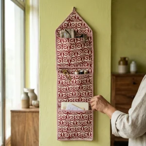 An interior room setup showing the Red Fabric Wall Hanging Organizer near a wooden desk, showcasing its space-saving capacity and elegant maroon room decor holder style.
