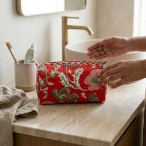 A traveler arranging the three pieces of the Red Floral Quilted Toiletry Bag Set on a modern bathroom vanity counter, displaying the large, medium, and small sizes filled with cosmetic brushes and skincare bottles.