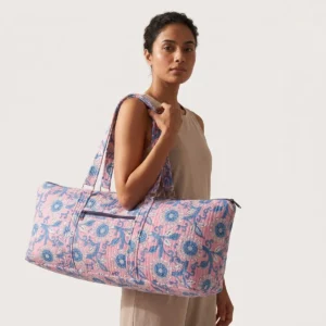 An outdoor studio scene featuring the Pink Floral Quilted Cotton Yoga Mat Bag held by its shoulder straps, highlighting its lightweight carrying convenience and bohemian style.